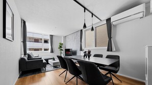 Una sala de estar moderna con comedor, un sofá gris, un televisor y un ventanal grande.