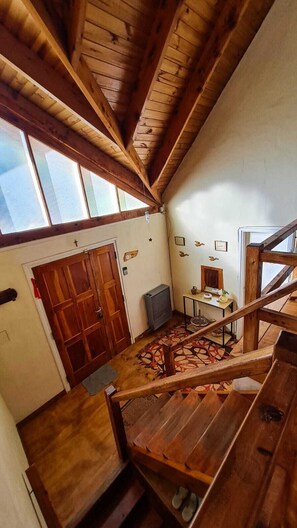 Un escalier en bois mène à une pièce dotée d’une grande fenêtre, d’une porte et d’une petite table sur laquelle se trouve un vase.
