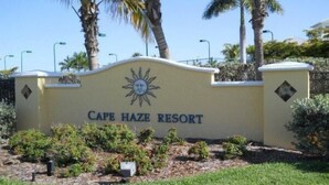 En skylt för Cape Haze Resort med en solsymbol, omgiven av grönska och palmer.