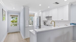 A modern kitchen with white cabinetry, a stainless steel refrigerator, a gas stove, and a gold faucet. - 2BR, 2BA Boca Grande condo with ocean views. (Boca Grande)