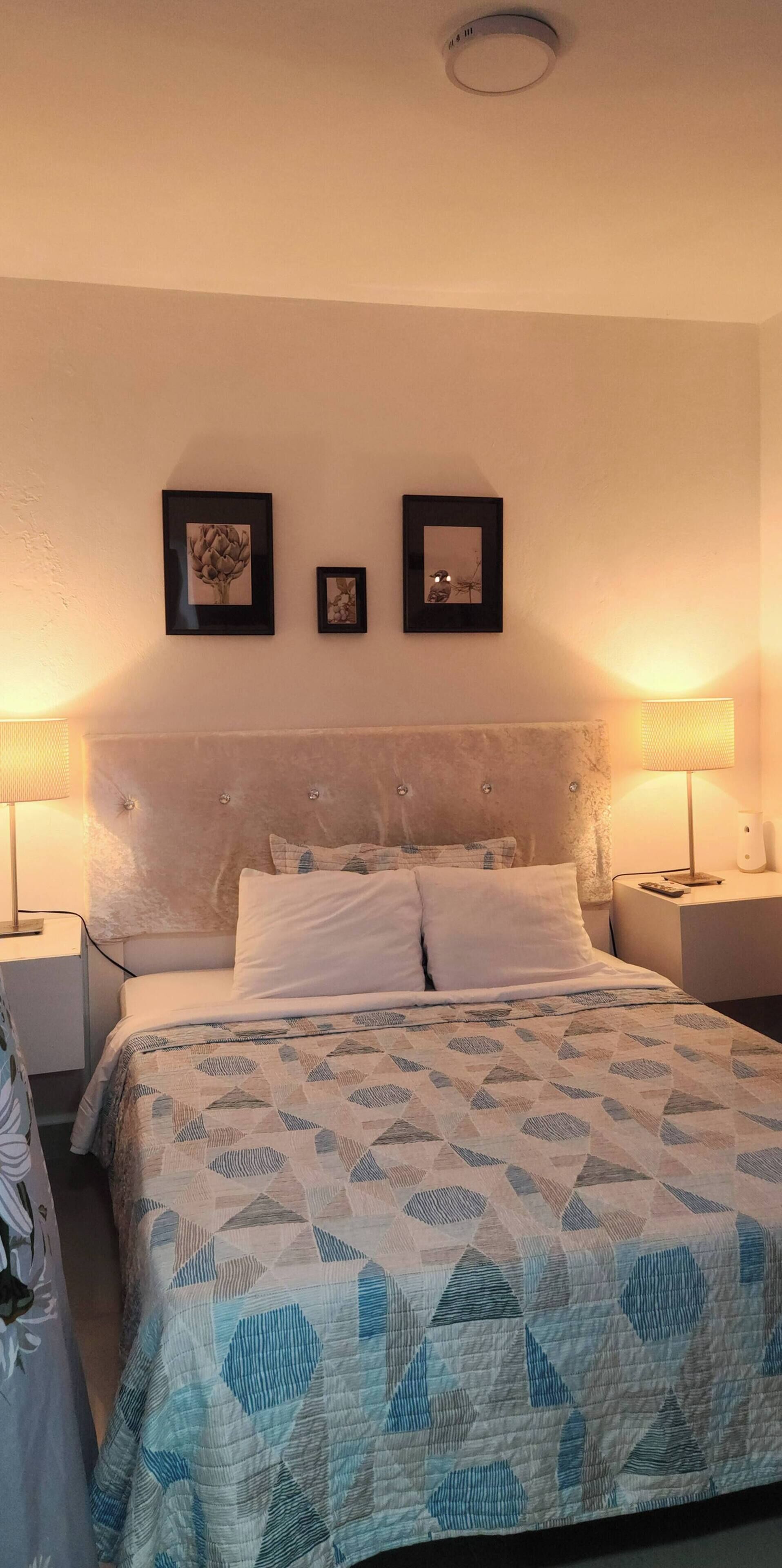 Een slaapkamer met een bed, twee nachtkastjes, een hoofdbord en foto's aan de muur.