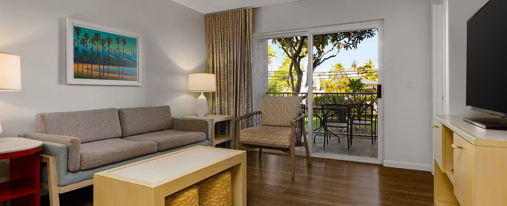 A living room with a sofa, a coffee table, a TV, a lamp, a chair, and a balcony with outdoor furniture.