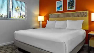 A hotel room with a bed, two bedside lamps, a nightstand, a window with blinds, and two wall-mounted pictures.