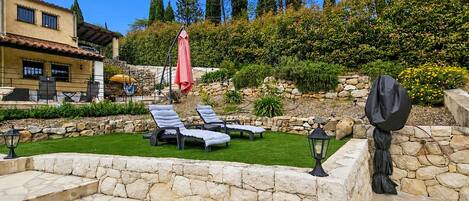 Een terras met stenen trappen, lounge fauteuils en een stenen muur.