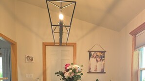 Ett matrum med ett träbord, mörka stolar, en bänk, en hängande lampa, en vas med blommor och en inramad tavla på väggen.