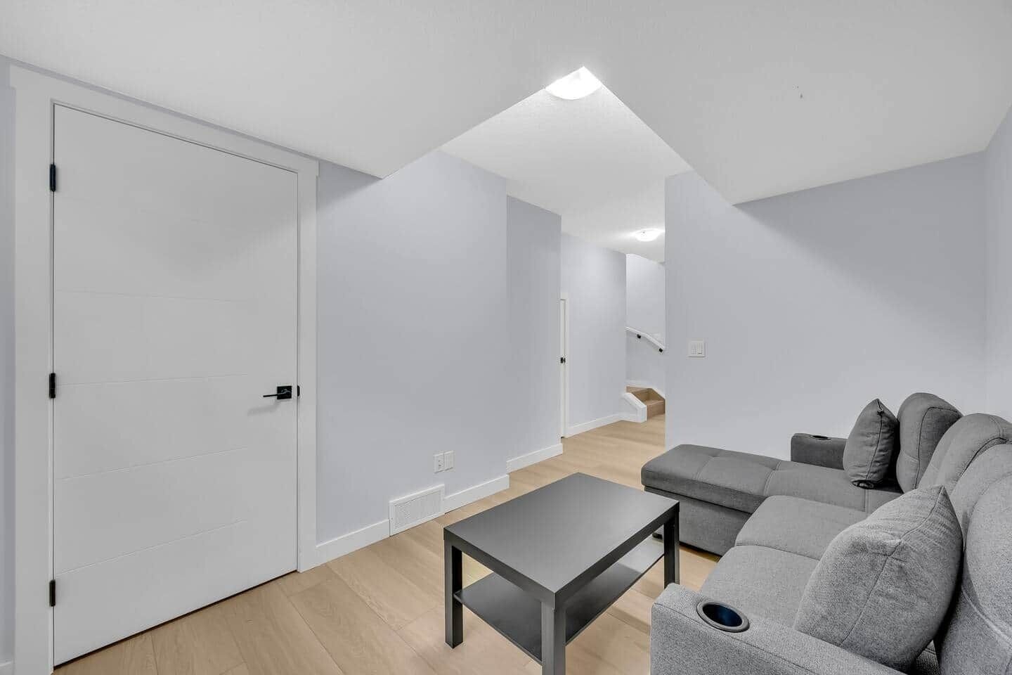 Una sala de estar moderna con un sofá gris, una mesita y una puerta blanca.