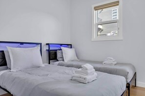 A hotel room with two beds, a window with blinds, and a neatly folded towel on the floor. - 301- City Skyline View (Calgary)