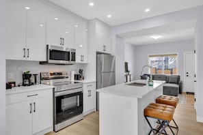 A modern kitchen with white cabinets, stainless steel appliances, and a central island with stools. - 301- City Skyline View (Calgary)