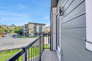 A balcony with a view of a multi-story building, a street, and parked cars. - 301- City Skyline View (Calgary)