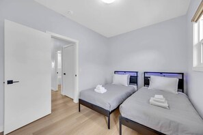 Une pièce avec deux lits, une porte donnant sur une autre pièce et un luminaire au plafond.