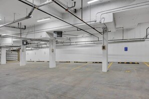 A spacious indoor parking area with concrete floors and white walls, featuring several pillars and a blue handicap parking sign. - 301- City Skyline View (Calgary)