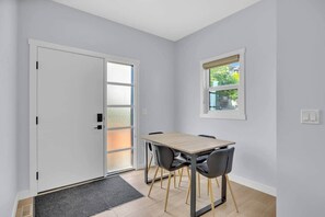Une pièce avec une porte blanche, une fenêtre donnant sur un beau paysage, une table avec des chaises et un petit tapis.