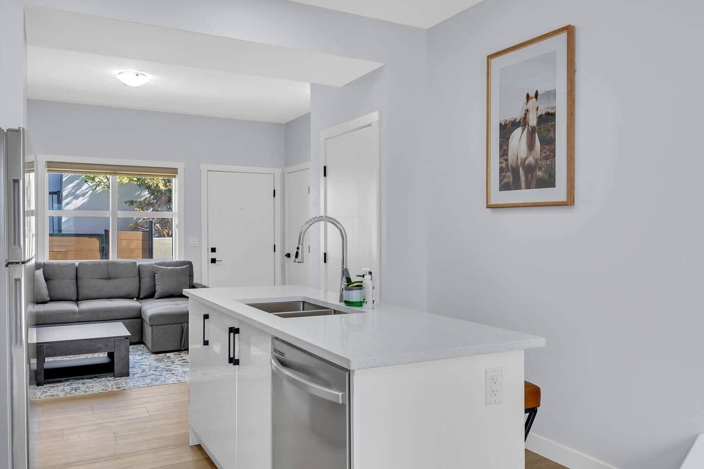 Una cucina moderna con un piano di lavoro bianco, lavastoviglie integrata e un'ampia finestra.