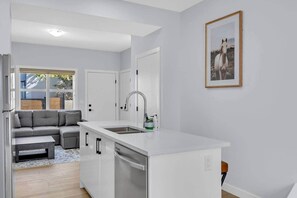 Eine moderne Küche mit weißer Arbeitsplatte, integriertem Geschirrspüler und großem Fenster.