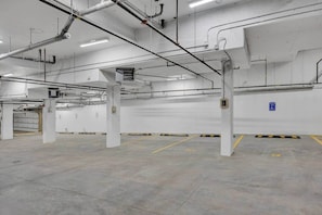 A spacious indoor parking area with concrete floors and white walls, featuring several pillars and a blue handicap parking sign. - Crescent Heights Retreat (Calgary)