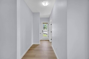 En smal hall med vita väggar och trägolv, som leder fram till en dörr med ett glasparti.