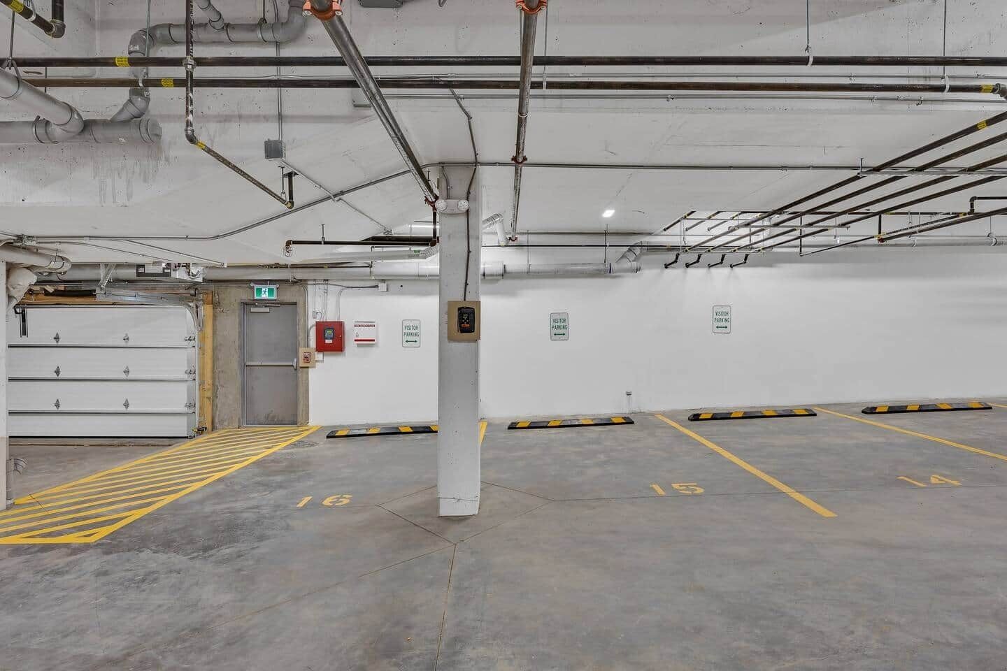 A parking garage with marked parking spaces, a fire extinguisher, and a visitor parking sign.