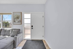 Ein modernes Wohnzimmer mit einem grauen Sofa, einer Tür mit mattiertem Glas und einer Topfpflanze an der Wand.