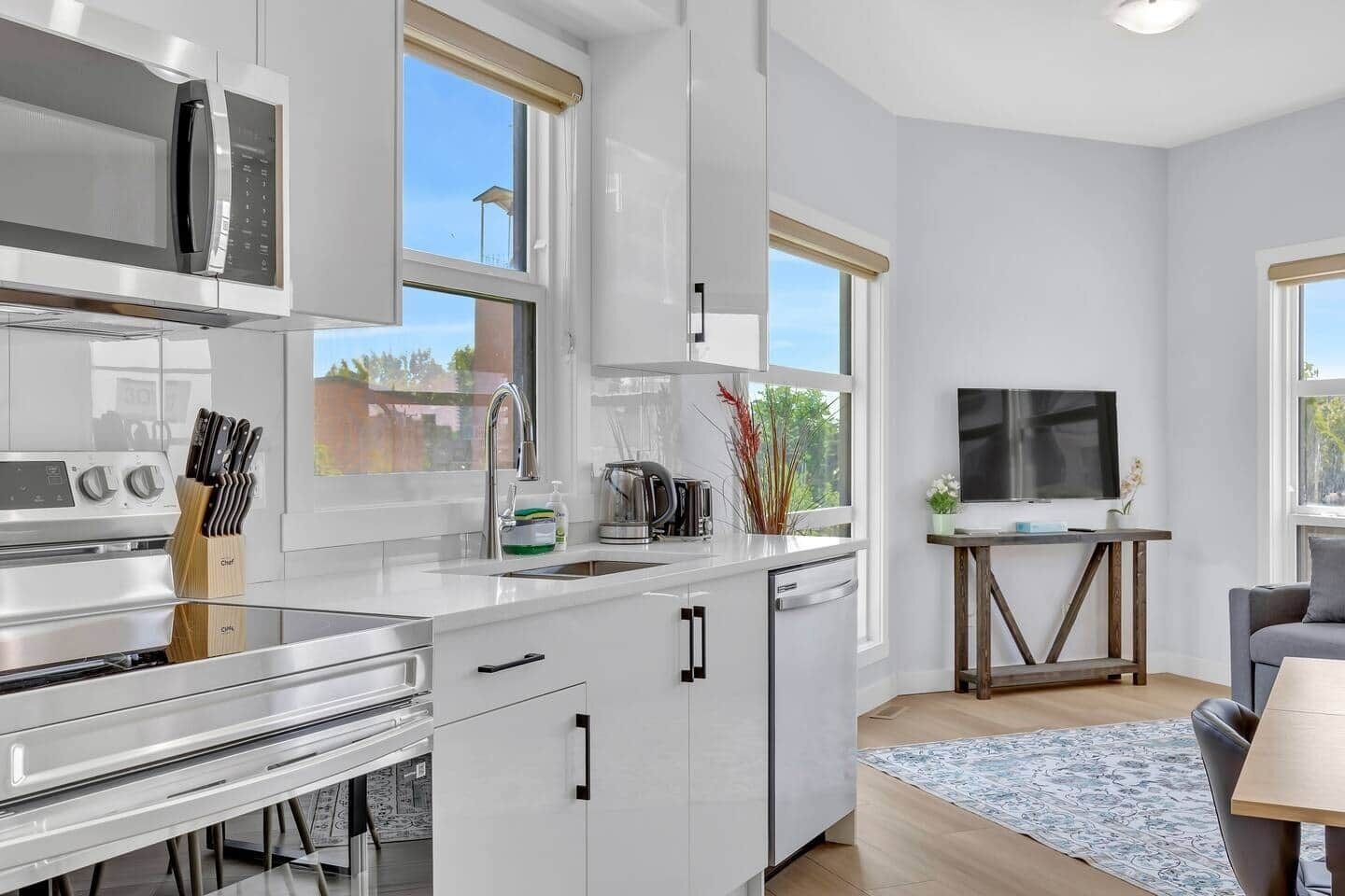 A modern kitchen with a built-in stove, a microwave, and a coffee maker. There is a dining area with a table and chairs, and a TV mounted on the wall.