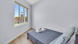Een slaapkamer met een enkel bed, een raam en uitzicht op een gebouw.