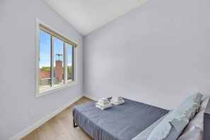 A bedroom with a single bed, a window, and a view of a building outside. - Crescent Heights Retreat (Calgary)