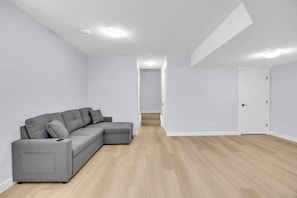 A modern, minimalistic living room with a grey sectional sofa, wooden flooring, and white walls. - Crescent Heights Retreat (Calgary)