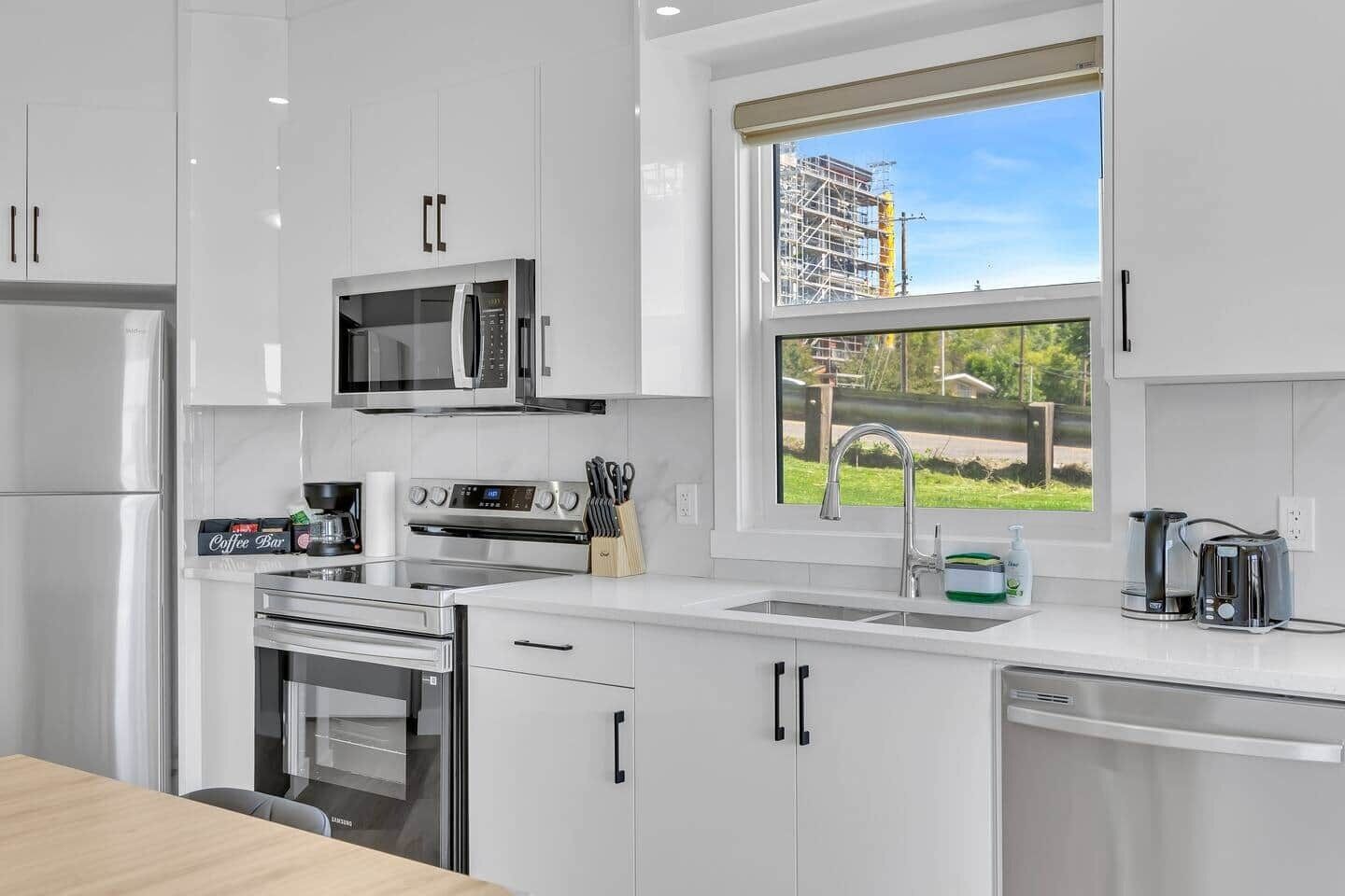 A modern kitchen with stainless steel appliances, a built-in microwave, and a window with a view of a construction site.