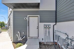 En byggnad med en grå fasad, en vit dörr och mätare för el, vatten eller gas på sidan.
