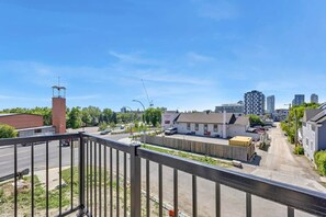 Eine Stadtansicht mit blauem Himmel, einer Straße mit Fahrzeugen und Gebäuden, darunter ein weißes Gebäude mit einem roten Schornstein.