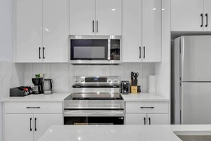 A modern kitchen with stainless steel appliances, white cabinetry, and a built-in oven. - Crescent Heights City view (Calgary)