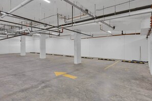A large, empty parking garage with concrete floors and walls, and numerous pipes and ducts on the ceiling. - Crescent Heights City view (Calgary)