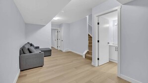 A spacious room with a grey sofa, wooden flooring, white walls, and a staircase leading to another level. - Crescent Heights City view (Calgary)