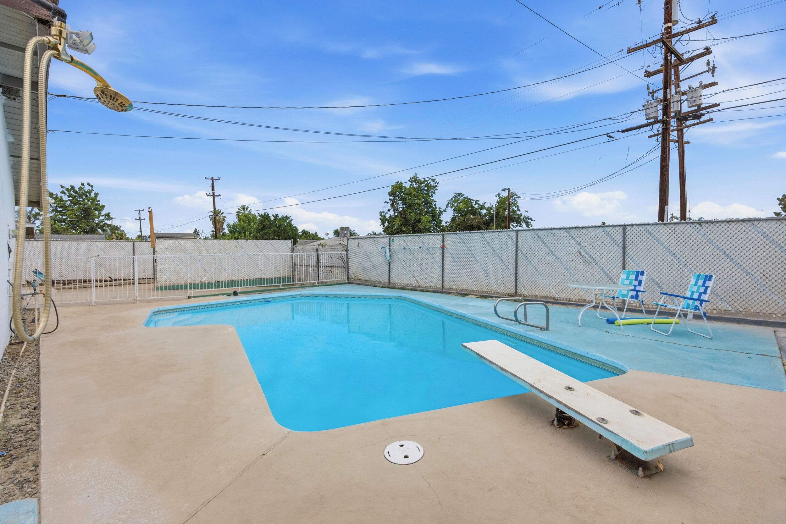 Una piscina con tabla de salto, rodeada por una valla, y una mesa con sillas.