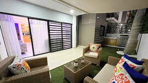 A modern living room with wicker furniture, a glass coffee table, and a view of the kitchen and balcony. - Family Comfort Apt, W/ Patio. BBQ/ Gym (Santiago de los Caballeros)