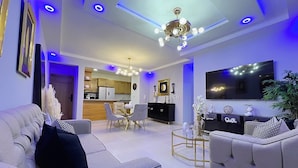 A modern living room with a sofa, a coffee table, a TV, and a dining area with chairs and a table. - Family Comfort Apt, W/ Patio. BBQ/ Gym (Santiago de los Caballeros)