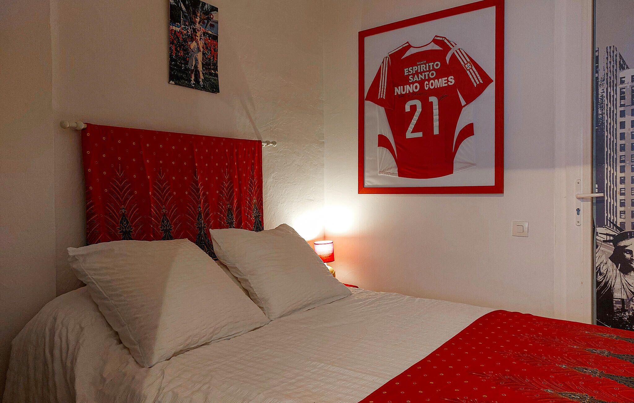 Un dormitorio con cama, almohadas, una cortina roja y una camiseta enmarcada en la pared.