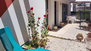 A patio with a white wall, a blue chair, a table with a white umbrella, and a potted plant with red flowers. - Stunning apartment in Royan with WiFi (Royan)