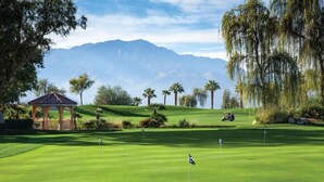 A golf course with a gazebo, palm trees, and mountains in the background.