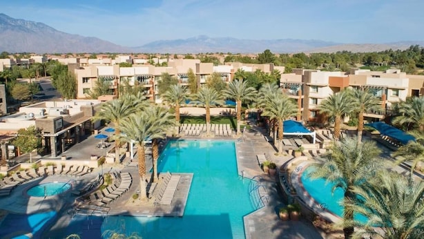 A resort with multiple swimming pools, palm trees, and a mountainous backdrop.