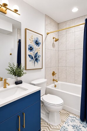 Ein Badezimmer mit einem weißen Waschbecken, goldenen Armaturen, einem blauen Schrank, einer Toilette, einer Badewanne und einer Dusche mit einem goldenen Griff.