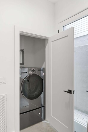 Ein kleiner Waschraum mit einer Waschmaschine mit Frontlader, einem Trockner und einer Tür zum Balkon.