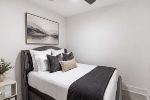 Ein Schlafzimmer mit einem Bett, einem Nachttisch, einer Zimmerpflanze und einem Bild an der Wand.