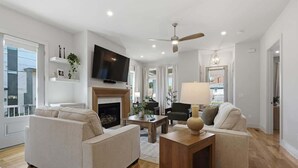 Un salon moderne avec une cheminée, des canapés, un téléviseur et un ventilateur de plafond.