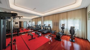Un gimnasio con cintas de correr, máquinas de pesas y colchonetas rojas.