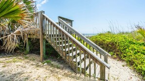 En trätrappa som leder ner till ett område vid stranden med sand och vegetation.