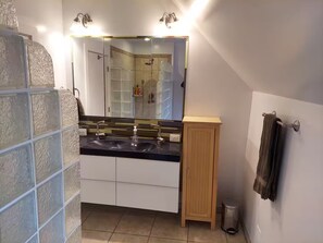 Kylpyhuone, jossa on lasiseinäinen suihkukaappi, peilillä varustettu pesuallas ja puinen kaappi.