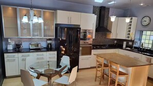 A modern kitchen with white cabinets, a black refrigerator, a wooden dining table, and a glass-top dining table.