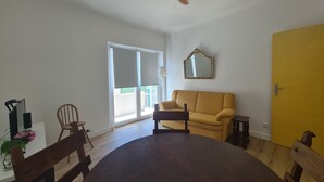 A room with a dining table, chairs, a sofa, a ceiling fan, a sliding glass door, and a yellow wall. - Lisbon Metro Yellow Line (Loures)