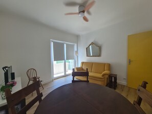A room with a dining table, chairs, a sofa, a ceiling fan, a sliding glass door, and a yellow wall. - Lisbon Metro Yellow Line (Loures)