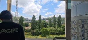 A person in a dark shirt with 'OGIPE' visible, looking out from a window with a view of a hill, trees, and a power line tower. - Lisbon Metro Yellow Line (Loures)